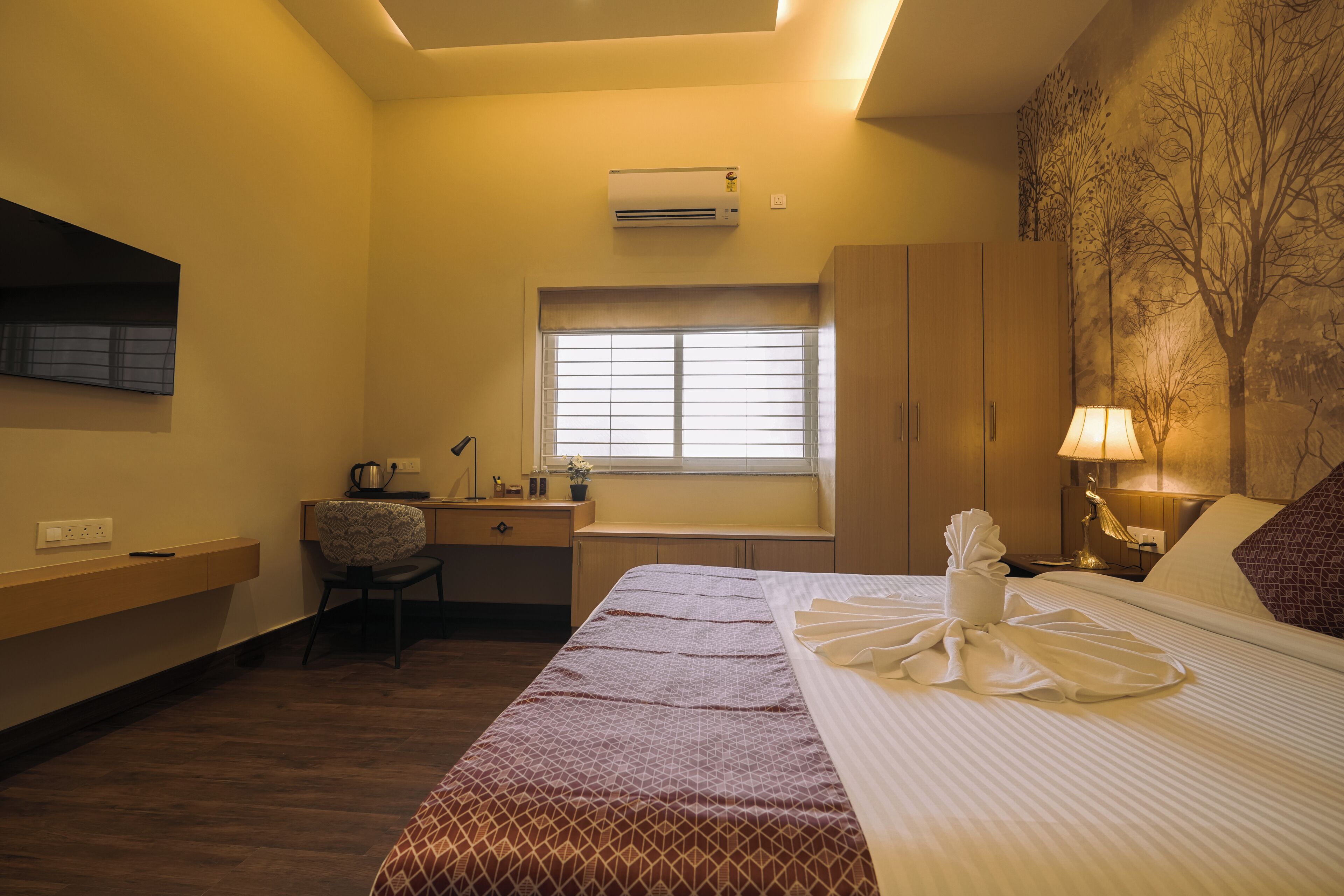 Una habitación de hotel con cama, escritorio, silla, ventana y aire acondicionado.