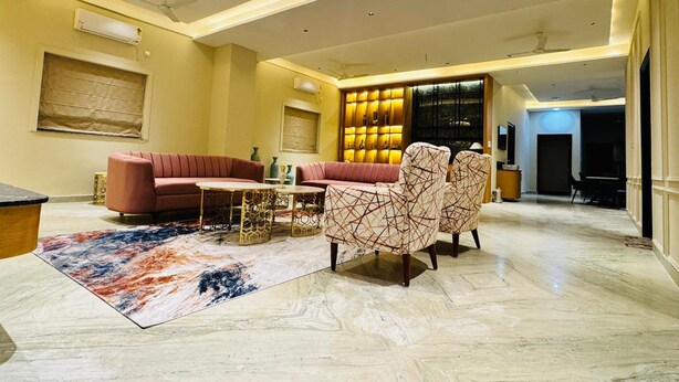 A spacious living room with a red sofa, patterned armchairs, and a marble floor. - The One Jubilee (Hyderabad)