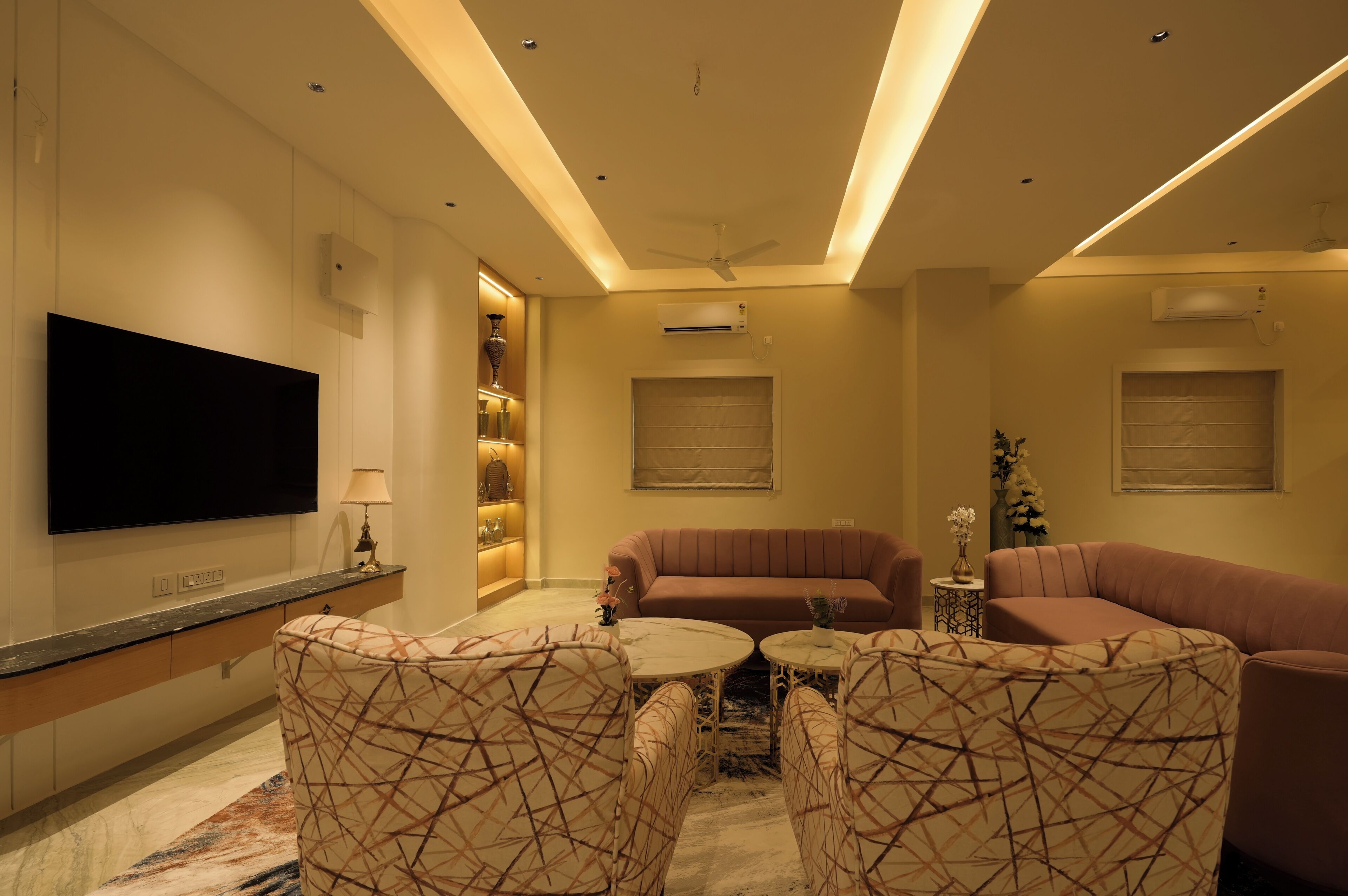 A modern living room with a flat-screen TV, two sofas, patterned chairs, a coffee table, and a decorative vase.