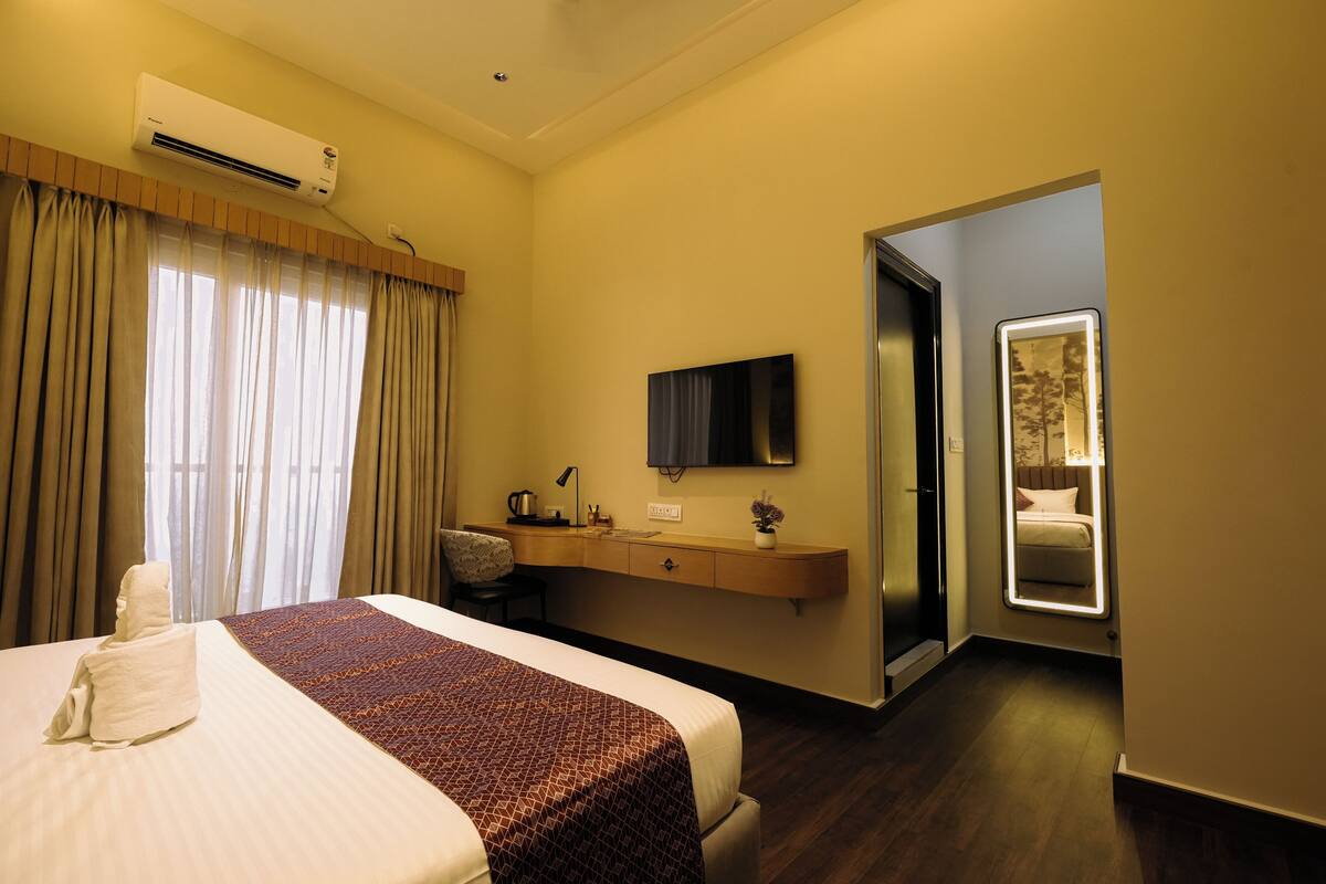 A hotel room with a bed, a desk, a chair, a flat-screen TV, and a mirror.