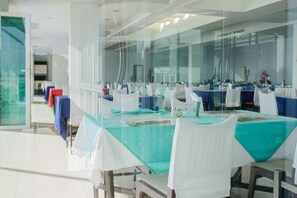 Un salón de conferencias con paredes de vidrio, sillas blancas y mesas cubiertas con manteles color turquesa.
