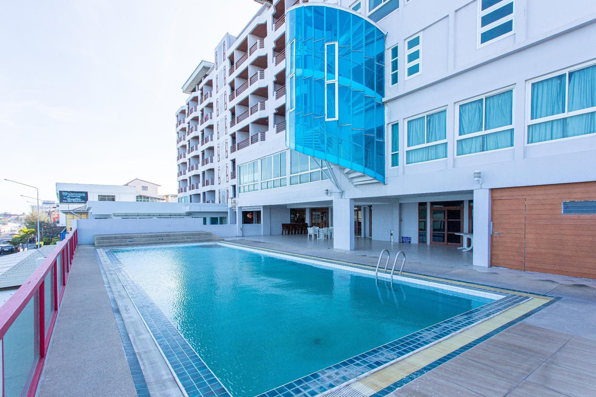 Un hotel con piscina, un área techada con mesas y sillas, y una fachada de edificio moderna.