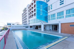 A hotel with a swimming pool, a covered area with tables and chairs, and a modern building facade. - Hadthong Hotel (Prachuap Khiri Khan)