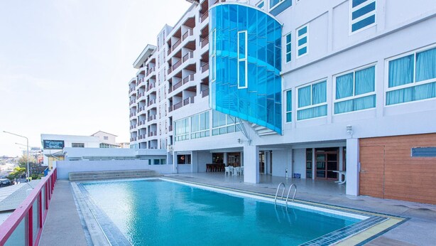 A hotel with a swimming pool, a covered area with tables and chairs, and a modern building facade. - Hadthong Hotel (Prachuap Khiri Khan)