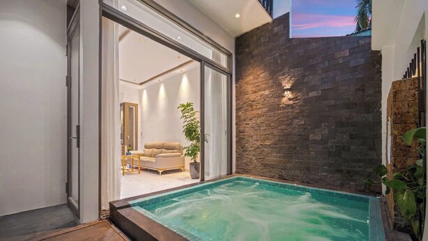 Una piscina moderna al aire libre con un muro de piedra y un ventanal de vidrio que da a una sala de estar.