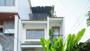Una casa moderna con puerta de madera, balcón y jardín con plantas verdes grandes.