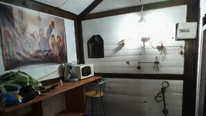 A small kitchen with a microwave, a coffee maker, and a wooden counter. There is a chair and a trash can.