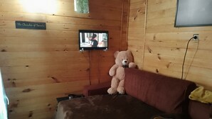 A wooden room with a bed, a television mounted on the wall, and a teddy bear on the bed.