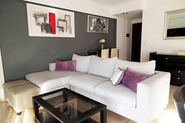 A modern living room with a sectional sofa, a glass coffee table, and abstract wall art.