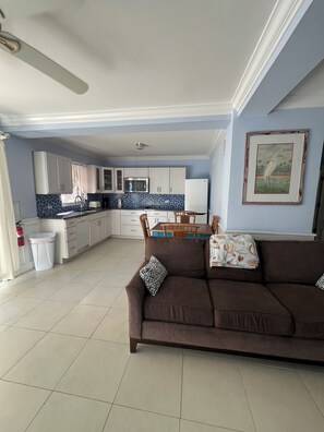A spacious living area with a brown sofa, a dining table, and a kitchen in the background. - Blue Sea Hideaway ~Perfect For Two 1-bedroom studio in quiet East End (East End)