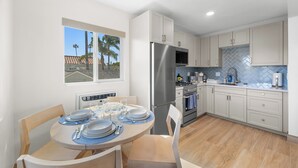 Una cocina moderna con armarios blancos, un refrigerador de acero inoxidable y un comedor con una mesa redonda para cuatro.