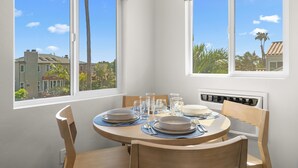 Comedor con una mesa dispuesta para cuatro personas, dos ventanas y vistas a edificios y árboles.