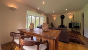 A dining area with a wooden table and chairs, a sofa, a television, and a fireplace. - Sanctuary in the Surrey Hills, Secluded Woodland Cottage, Walking Cycling Nature (Ranmore Common)