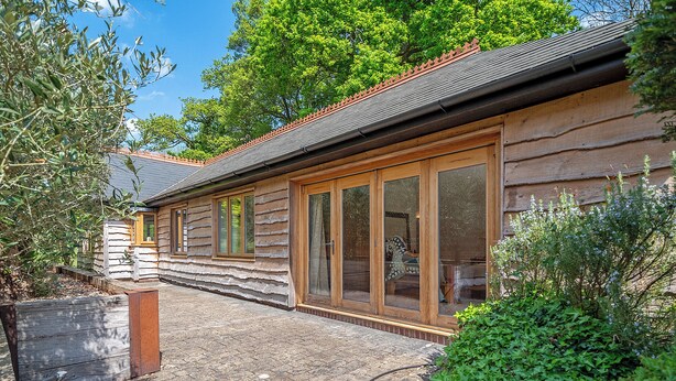 A log cabin with large windows and a stone pathway leading to the entrance. - Sanctuary in the Surrey Hills, Secluded Woodland Cottage, Walking Cycling Nature (Ranmore Common)