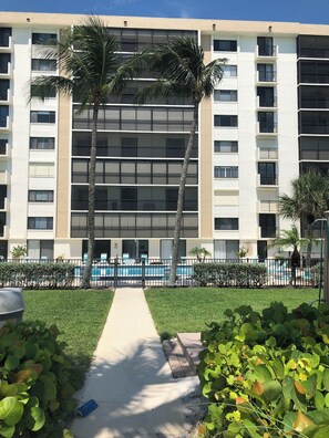 Ein mehrstöckiges Hotel mit Schwimmbad, Palmen und einem Weg zum Pool.