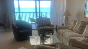 A living room with a sofa, armchair, and a glass coffee table. There is a view of the sea through large windows. - Beachfront location, magnificent views for an unforgettable serene escape (Naples)