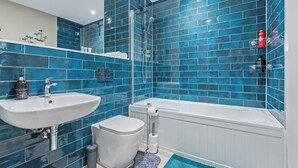 Ein Badezimmer mit blauen Fliesen, einem weißen Waschbecken, einer Toilette und einer Badewanne.