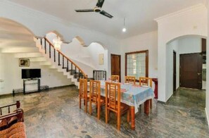 A dining area with a table set for four, a staircase, and a television on a stand. - Wayanad Inns Serviced Villa (Thrikkaipatta part)