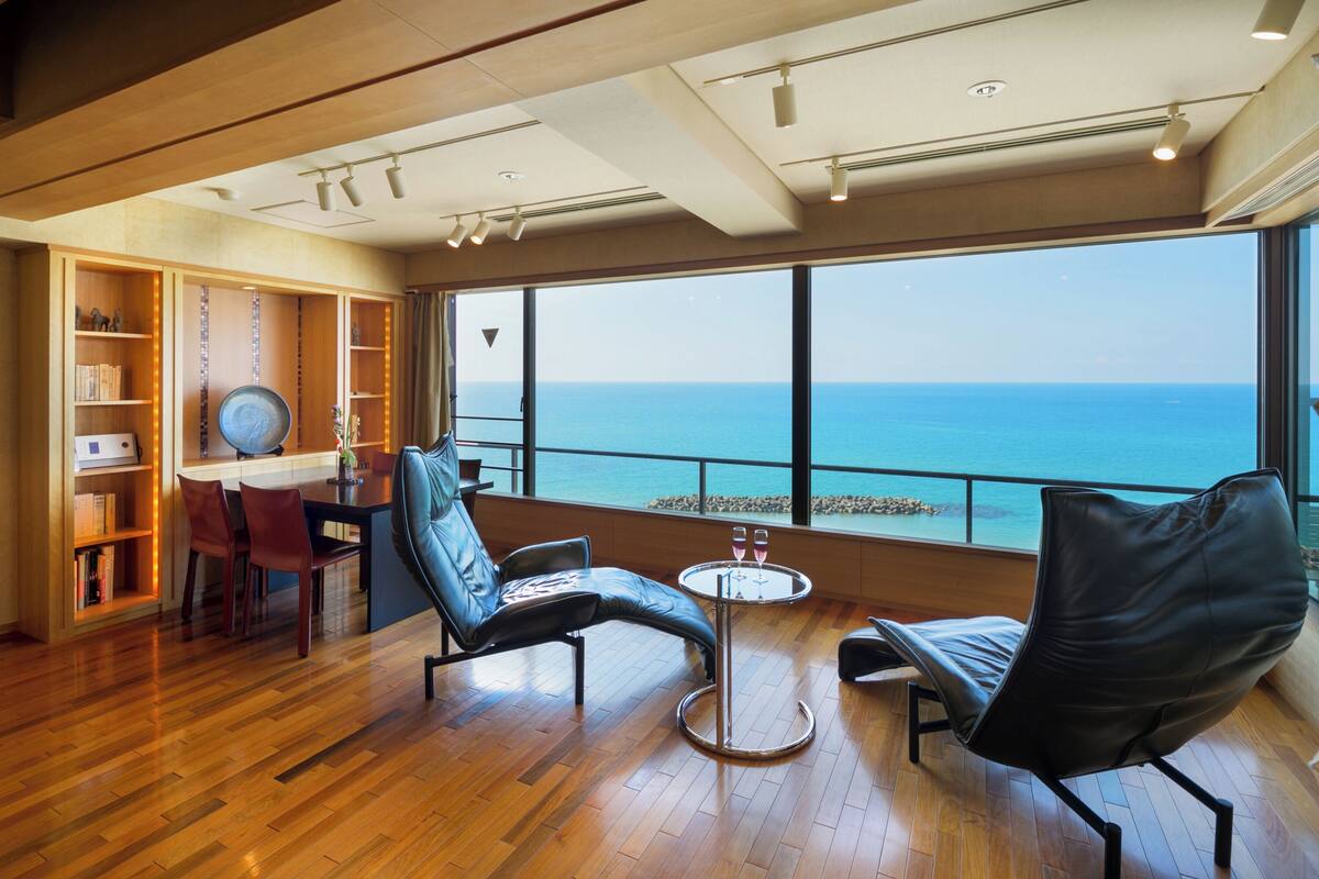 Une chambre moderne avec un plancher en bois, un coin repas, un espace salon avec vue sur la mer et une bibliothèque.