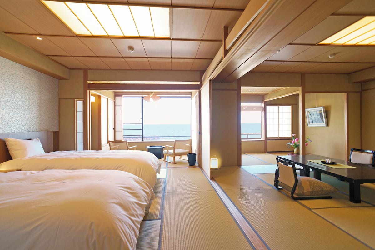 Une chambre d’hôtel avec deux lits, un coin salon avec une table et des chaises, et une vue sur la mer.