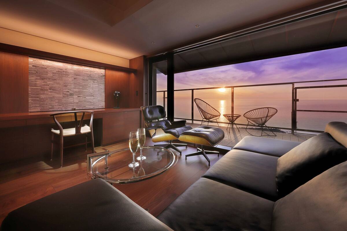 Un intérieur moderne avec une table en verre, des sièges en cuir et une vue sur le coucher de soleil sur l’eau.