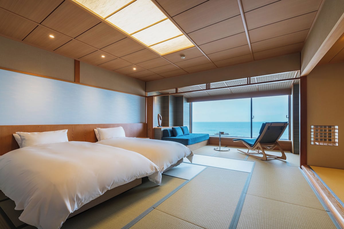 Une chambre d’hôtel avec deux lits, un coin salon donnant sur la mer et une grande fenêtre.