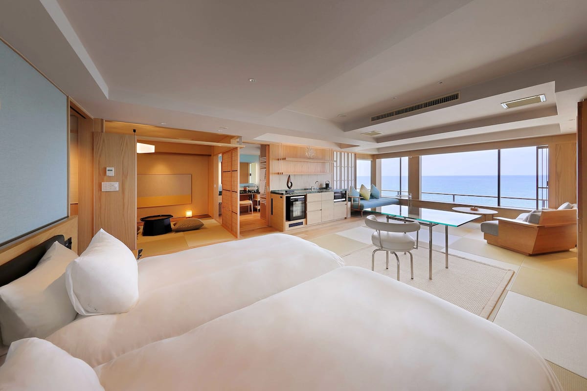 Une chambre d’hôtel moderne dotée d’un grand lit, d’un coin repas et offrant une vue sur la mer.