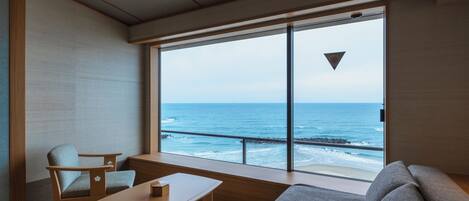 A modern room with a large window overlooking the ocean, a sofa, a table, and a chair.