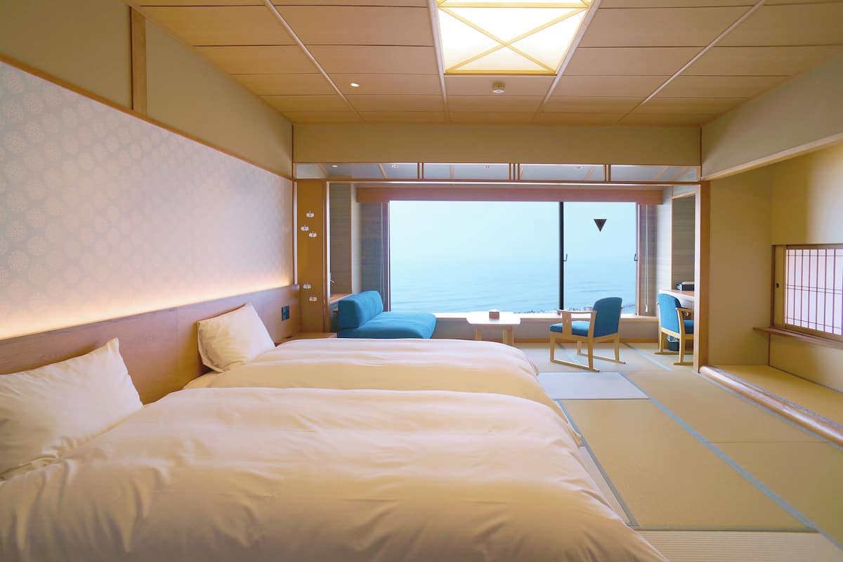Une chambre d’hôtel dotée d’un grand lit, d’un coin salon avec vue sur la mer et d’une porte coulissante donnant sur le balcon.