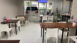 A clean, modern dining area with white chairs and tables, a television mounted on the wall, and a view of the street outside. - The Campus (Khlong Luang)