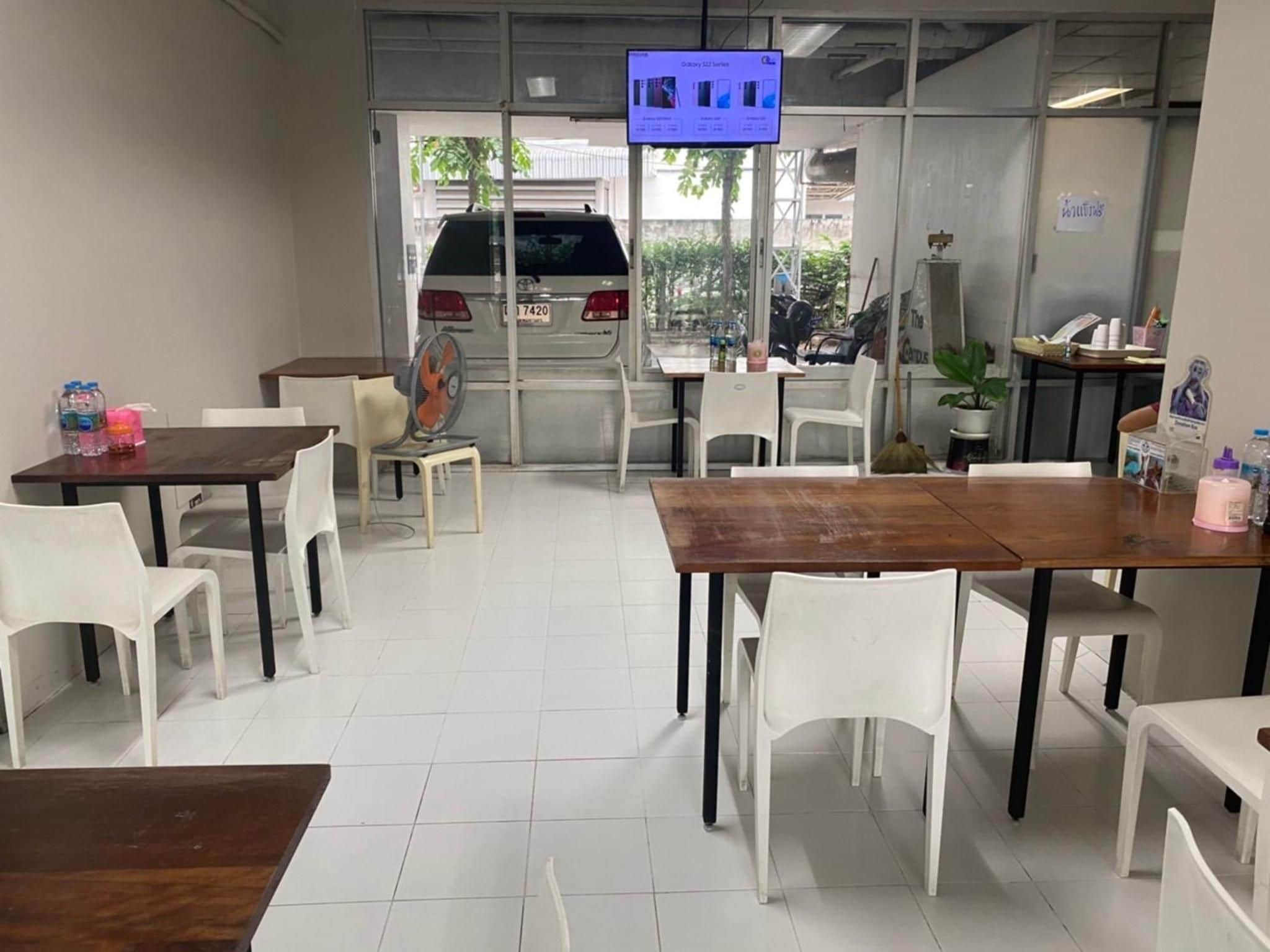 A clean, modern dining area with white chairs and tables, a television mounted on the wall, and a view of the street outside.
