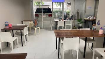 A clean, modern dining area with white chairs and tables, a television mounted on the wall, and a view of the street outside.