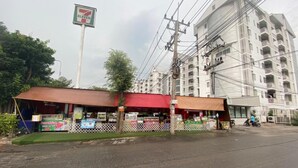 A 7-Eleven convenience store with a red roof, surrounded by a fenced area with various advertisements. - The Campus (Khlong Luang)