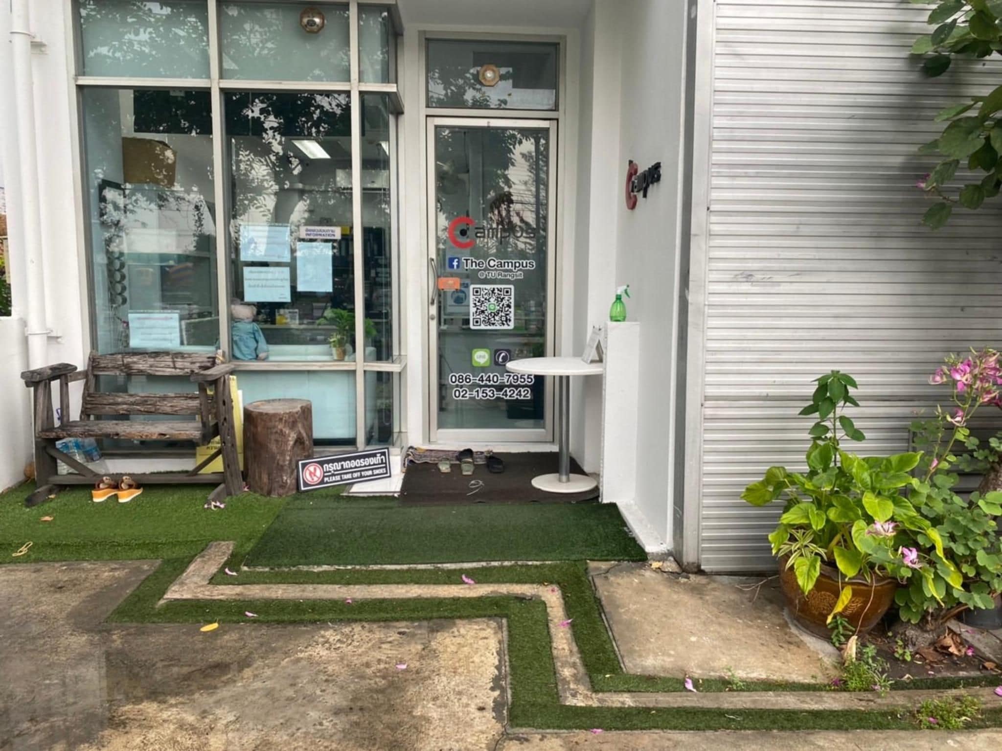 A small shop with a glass door, a wooden bench outside, and a small table with a spray bottle.