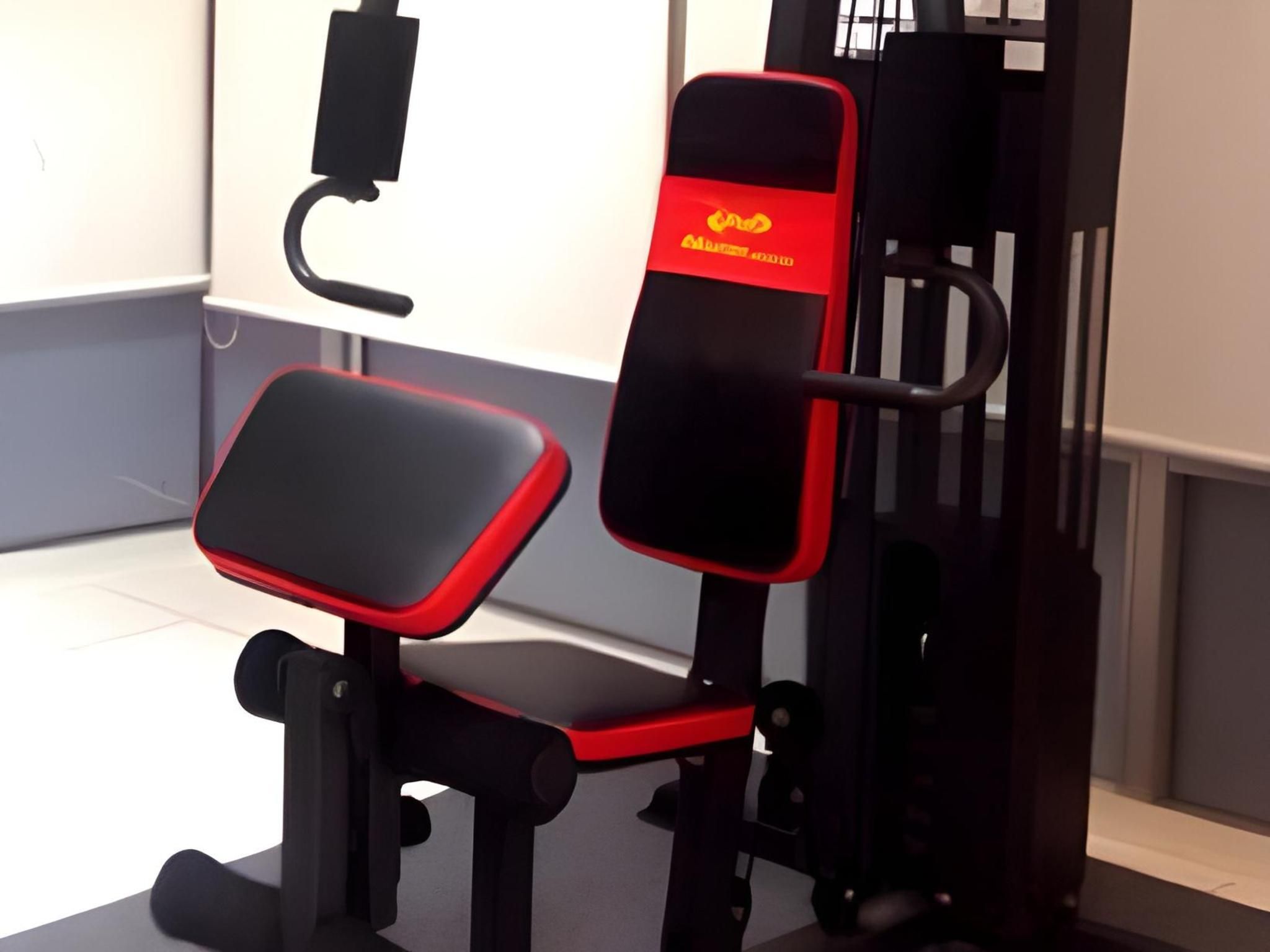 A gym with a red and black exercise machine, a pull-up bar, and a white wall in the background.