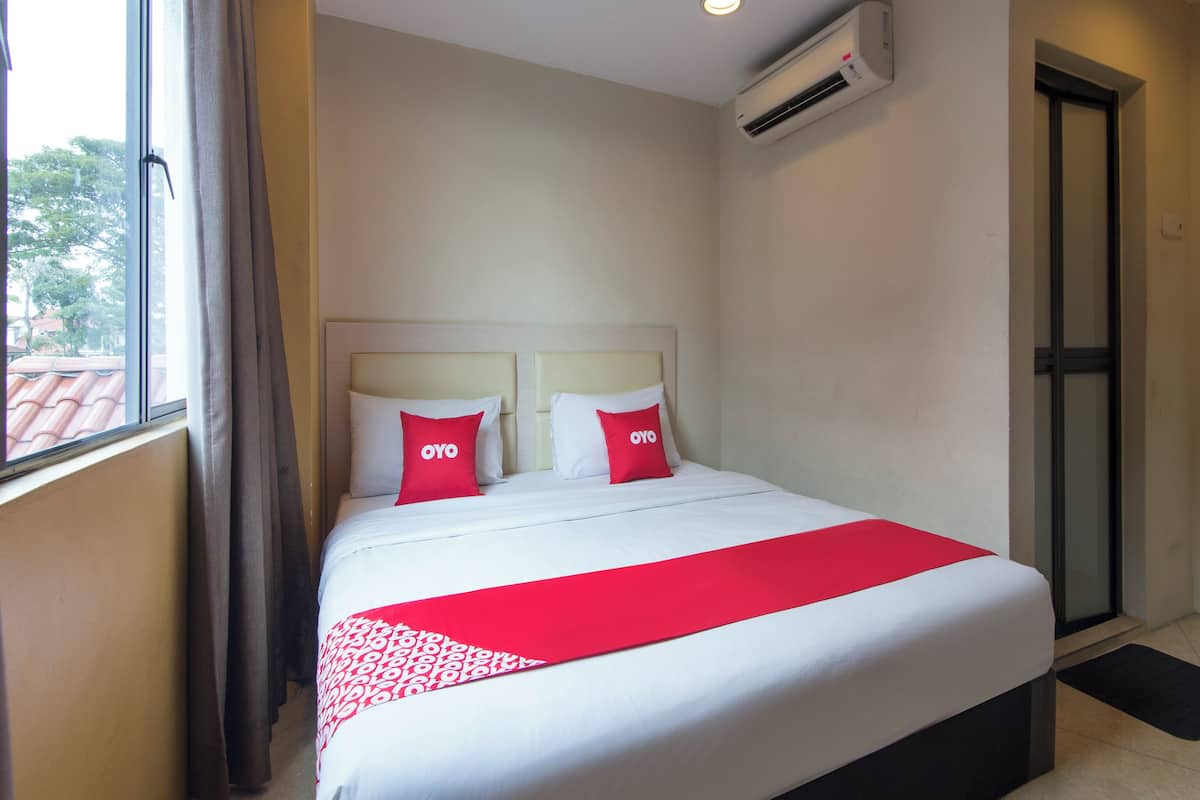 A hotel room with a bed, two pillows with 'OYO' branding, an air conditioning unit, a window with curtains, and a door.