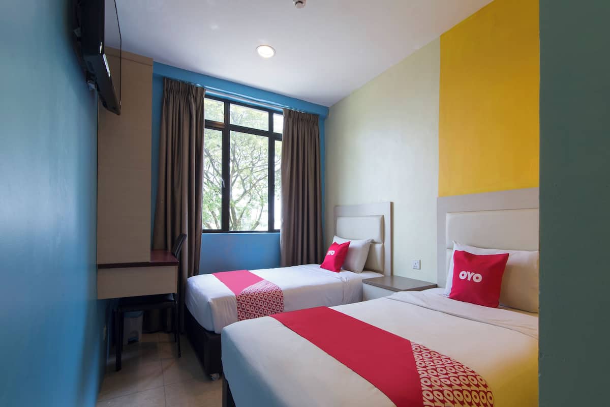 A hotel room with two beds, a desk, and a window with curtains.
