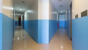 A long, narrow hallway with blue and white walls, tiled floors, and directional signs. - Hotel 916 (Batu Caves)