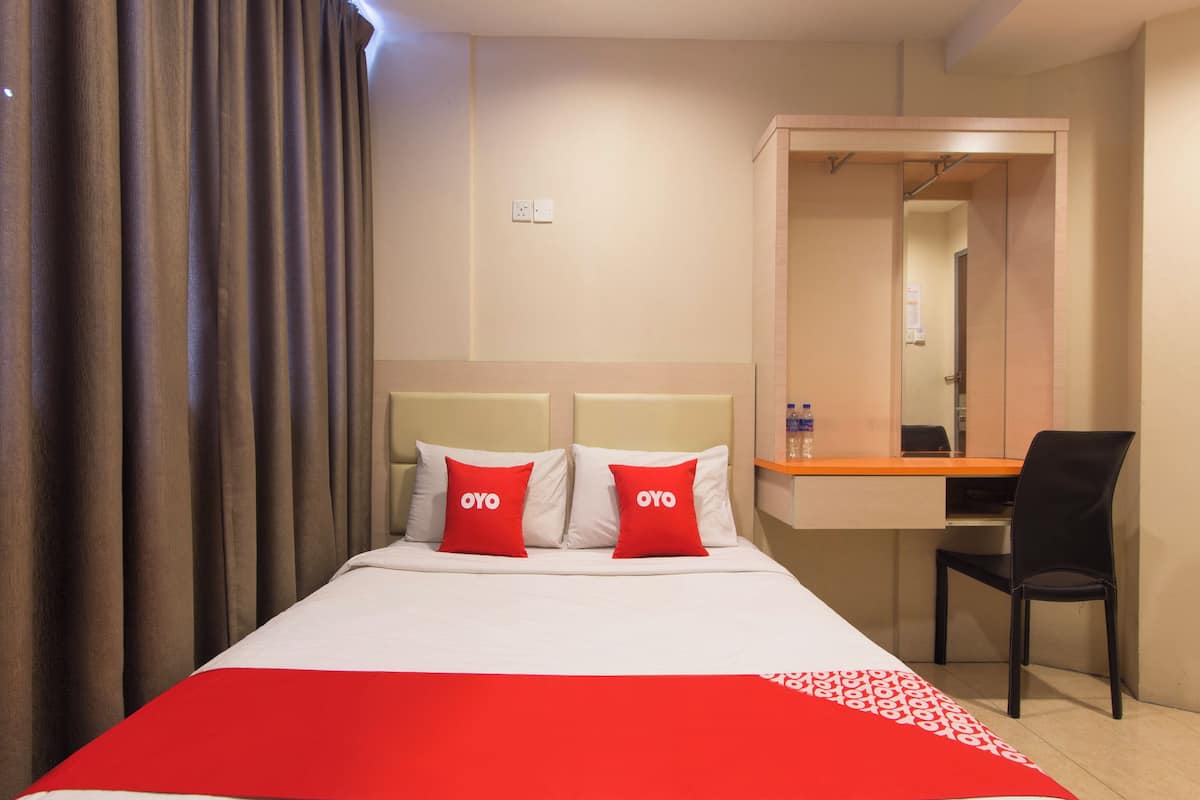 A hotel room with a bed, two red pillows with "OYO" branding, a desk with a chair, and a mirror.