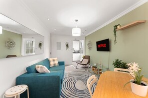 Ein modernes Wohnzimmer mit einem türkisfarbenen Sofa, einem Holzesstisch und einem an der Wand befestigten Fernseher.