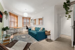 Ein modernes Wohnzimmer mit einem türkisfarbenen Sofa, einem Glastisch und einem Essbereich mit weißem Tisch und Stühlen.
