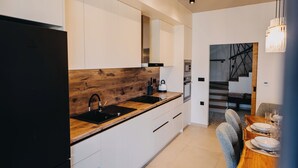 Eine moderne Küche mit weißen Schränken, einer Holzarbeitsplatte und einem schwarzen Spülbecken. Es gibt einen Essbereich mit einem Tisch für zwei Personen und eine Treppe im Hintergrund.