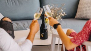 Zwei Personen sitzen an einem Tisch mit einer Weinflasche und Gläsern.