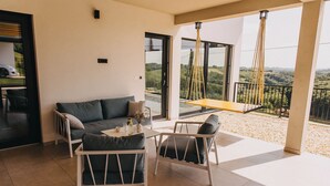 Ein modernes Wohnzimmer mit einer Couch, zwei Sesseln und einem Tisch. Ein großes Fenster bietet Blick auf die Landschaft.