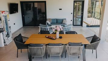 A modern dining area with a wooden table and wicker chairs, a sofa with cushions, and a hanging swing chair.