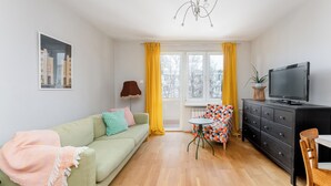 Un salon avec un canapé, une petite table, un téléviseur et une fenêtre ornée de rideaux jaunes.