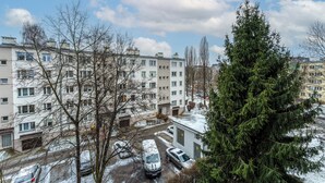 Un quartier résidentiel avec des immeubles à plusieurs étages, des voitures garées et un grand arbre à feuilles persistantes.