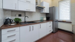 Une cuisine moderne avec des meubles blancs, un réfrigérateur en acier inoxydable, un évier et une fenêtre équipée de stores.