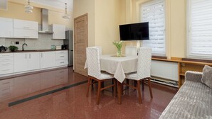 Une cuisine moderne avec des meubles blancs, une table à manger avec des chaises, un téléviseur et une fenêtre avec des stores.