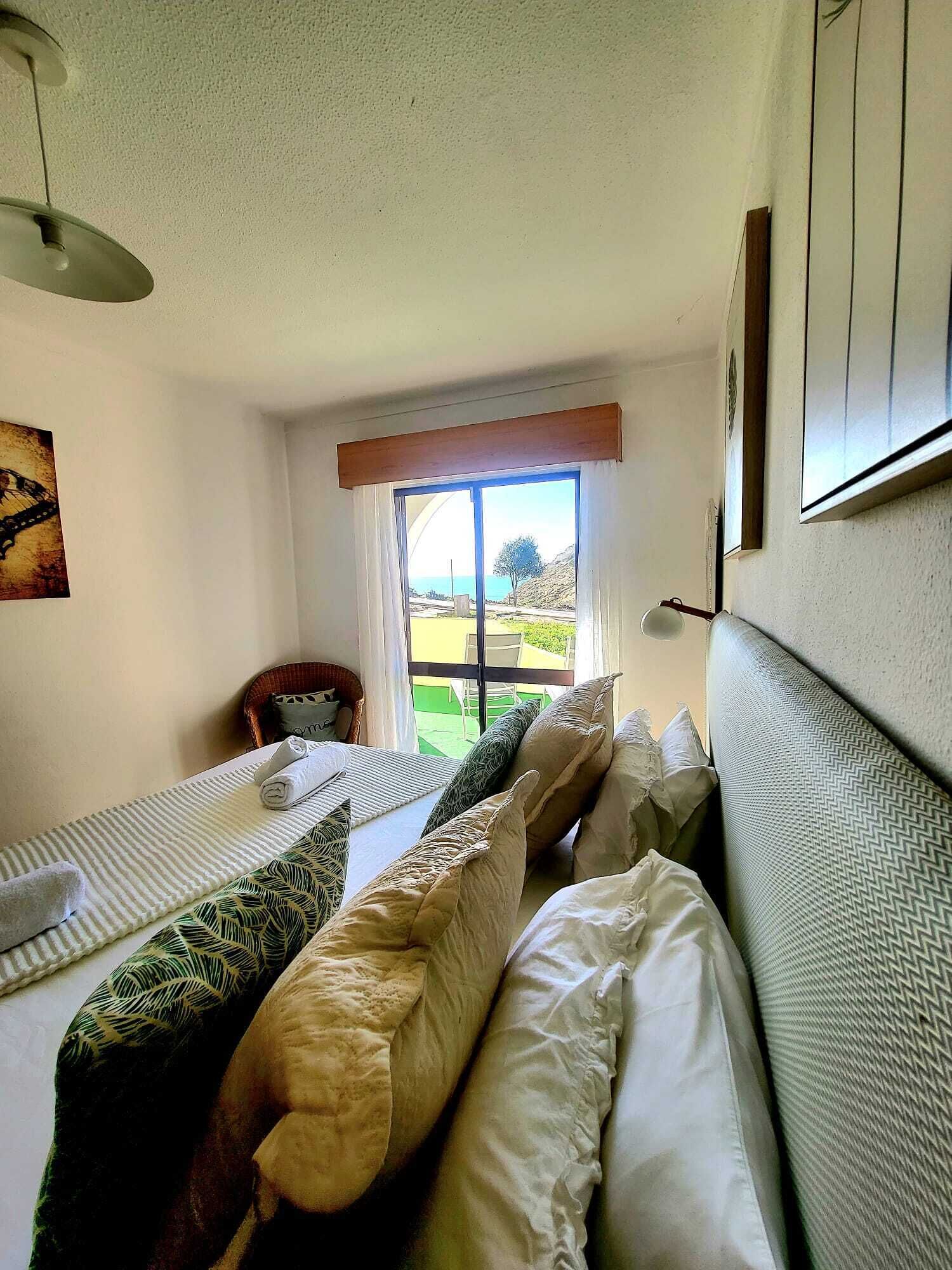 Une chambre avec deux lits, une fenêtre donnant sur un beau paysage, un ventilateur de plafond et un tableau au mur.